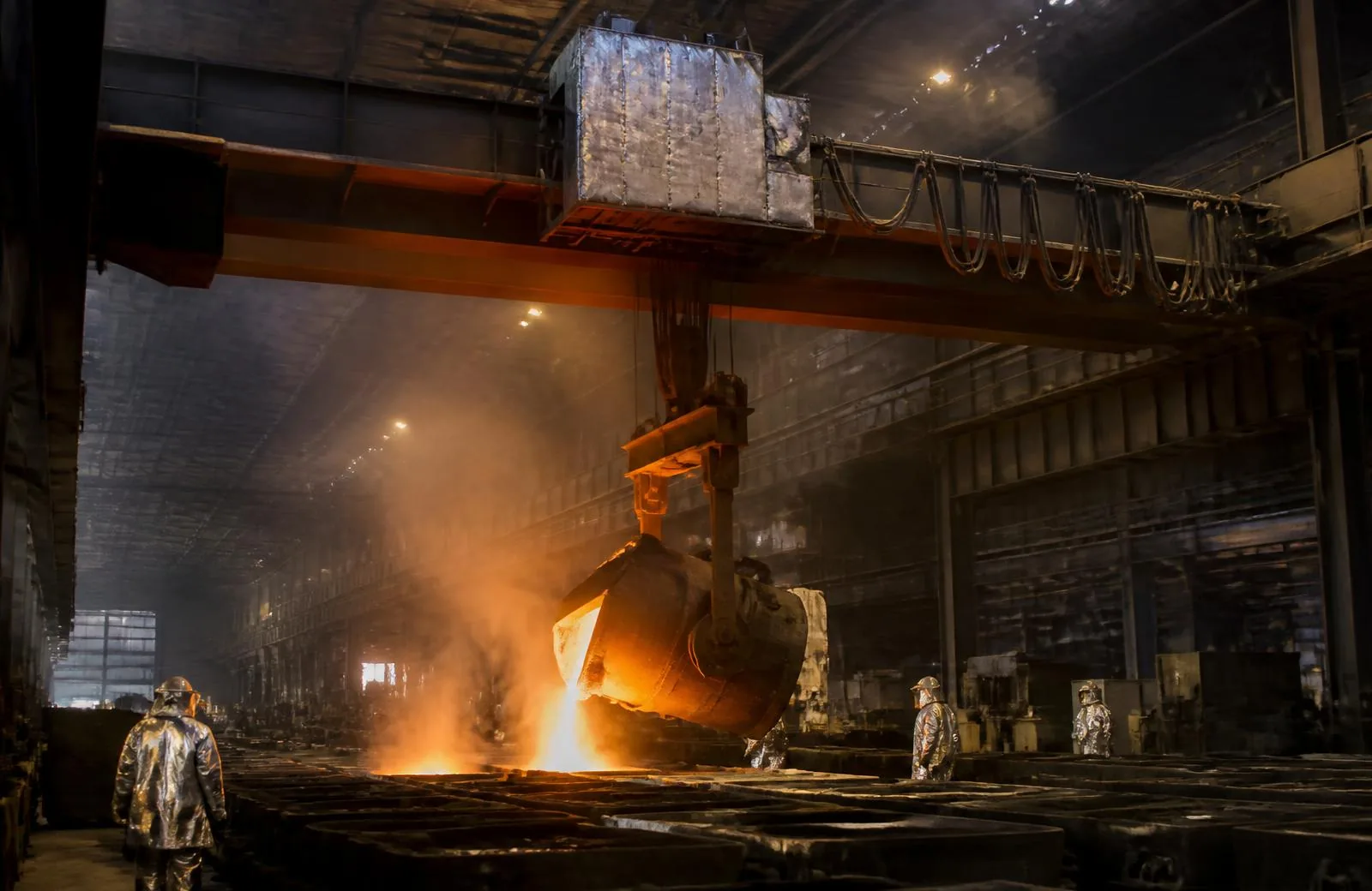 Foundry crane with heat-shielded trolley pouring molten metal into sand moulds