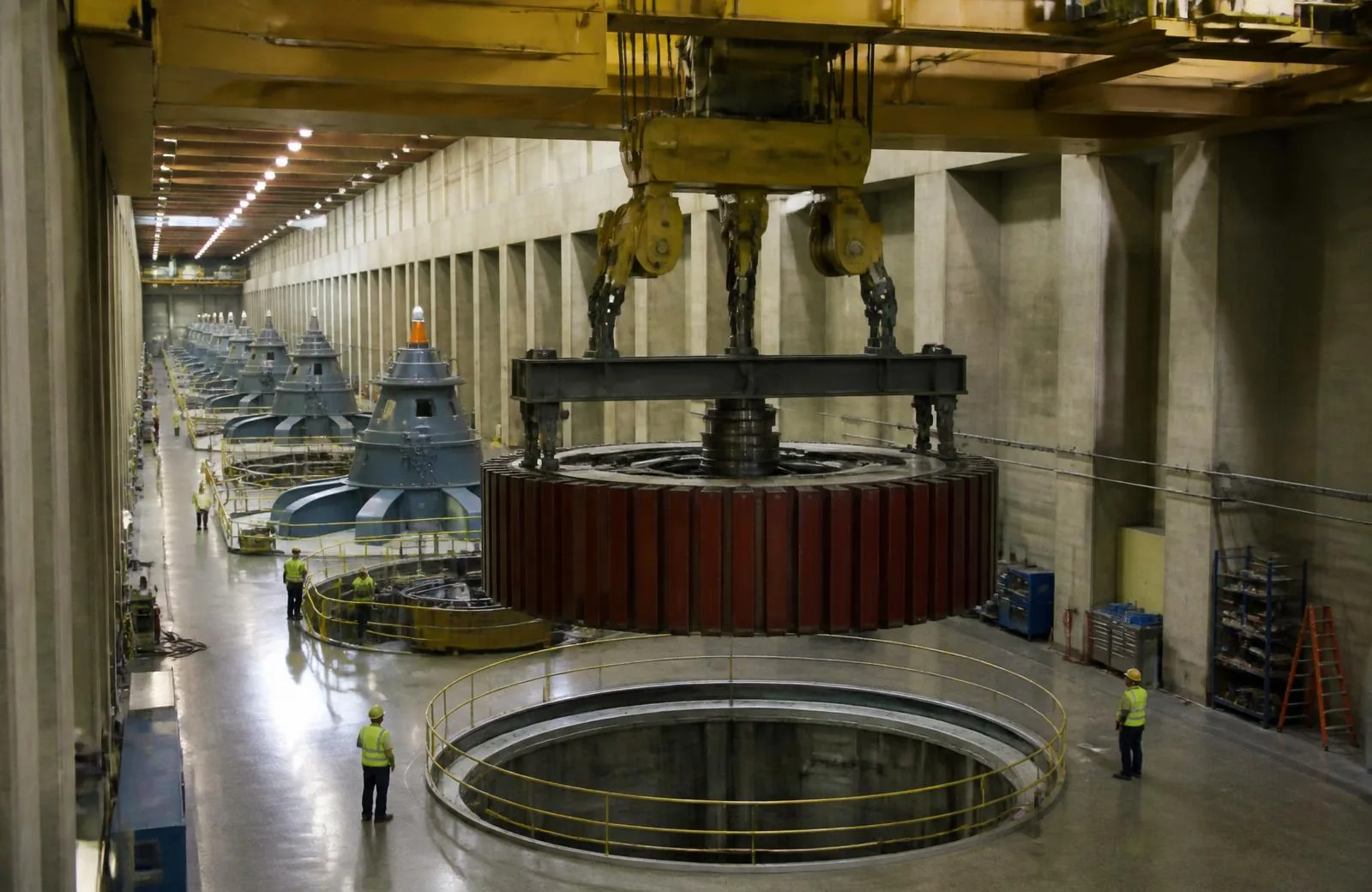 Hydroelectric powerhouse crane lifting a generator rotor with a heavy lifting beam above a generator pit