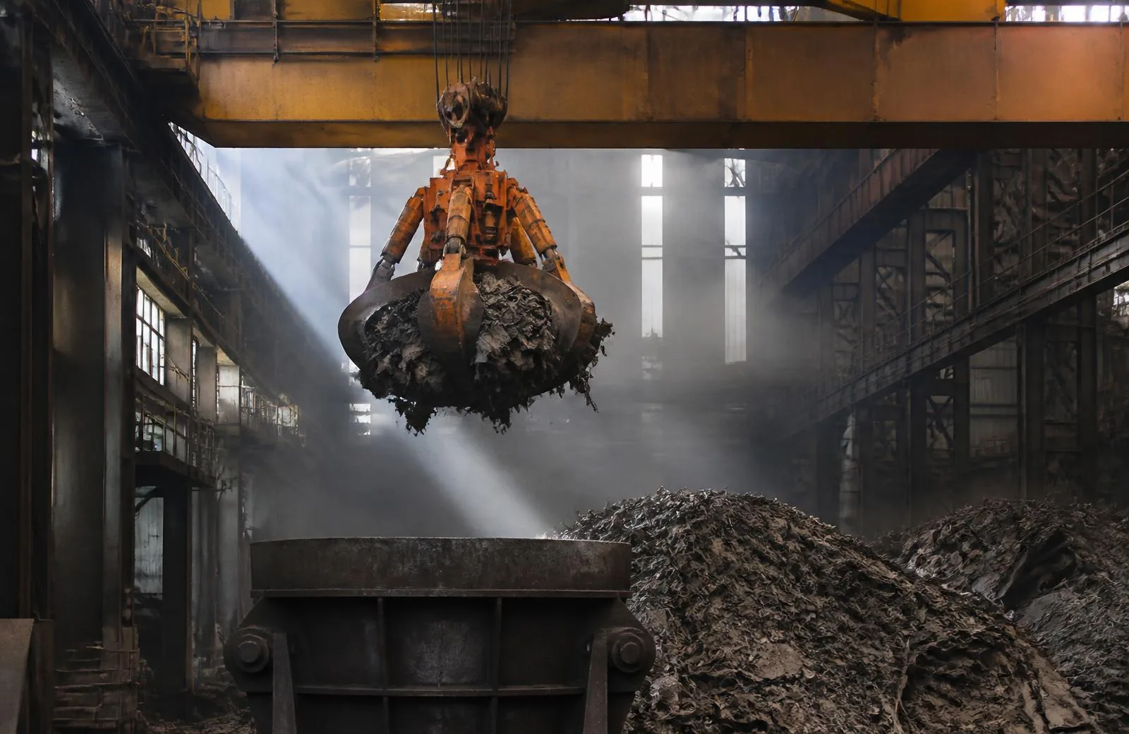 Scrap-handling overhead crane with orange-peel grab loading a charging bucket